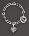 An edgy charm bracelet centered on a chunky sterling silver bracelet with etched heart pendant. Designed by Lagos.