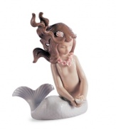 The world is her oyster. A pretty young mermaid treasures a shiny pearl in this fanciful porcelain figurine from under the sea, handcrafted by Lladro.