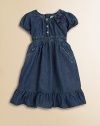 An adorable denim day dress accented with a darling floral detail and silvertone snaps.Jewel necklineCap sleeves with elasticized cuffsFront snap placketConcealed back zip closureElasticized waistbandSide slash zip pocketsRuffle hem65% cotton/35% polyesterMachine washImported