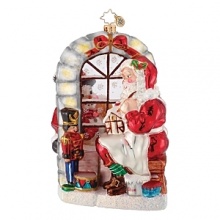 Santa crafts Christmas toys under the watchful eye of a nutcracker in this festive glass ornament.