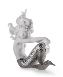 A dramatic, silver mermaid tail makes this unique piece from Lladro truly stunning. Decorated with delicate shell and flower jewelry, the underwater beauty lounges in princess-like majesty at the bottom of the sea. 6.5 x 5.25.